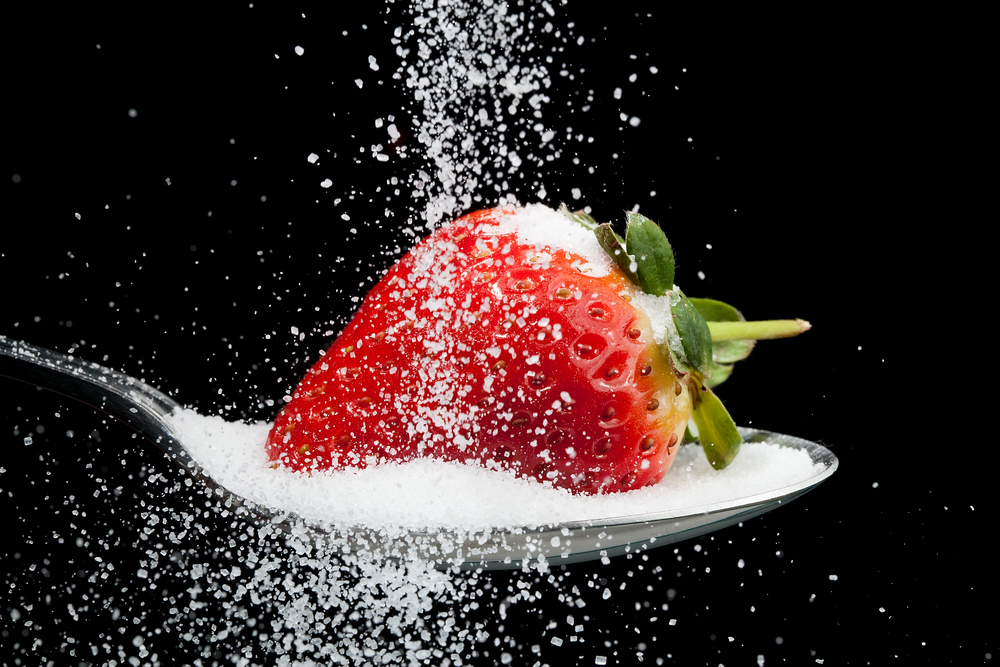 Sugar being poured over strawberry that is sat in sugar on a spoon. This is to represent the amount of sugar in fruit